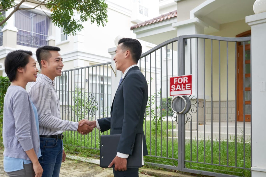 A real estate agent shaking hands with a couple in front of a property for sale