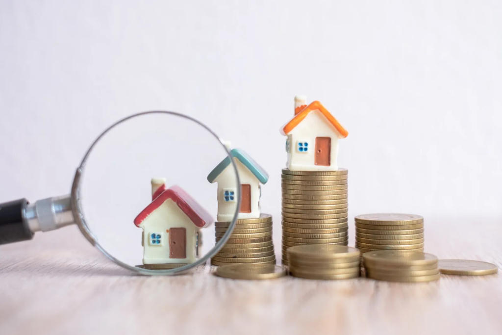 Miniature houses on stacks of coins being viewed through a magnifying glass, representing the concept of evaluating is Bulacan a good investment?