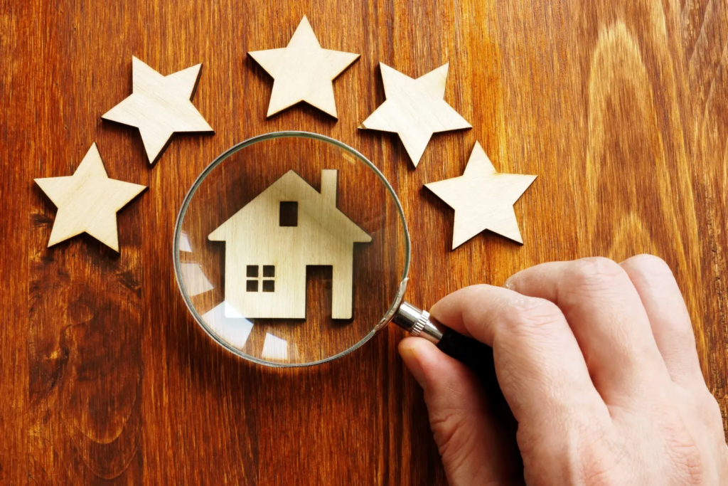 A hand holds a magnifying glass over a wooden house cutout, surrounded by six wooden stars. The image suggests analyzing real estate investment opportunities in Bulacan.